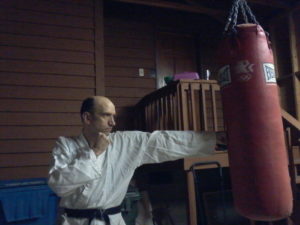 Jim in his white karate uniform and black belt, punching a large punching bag