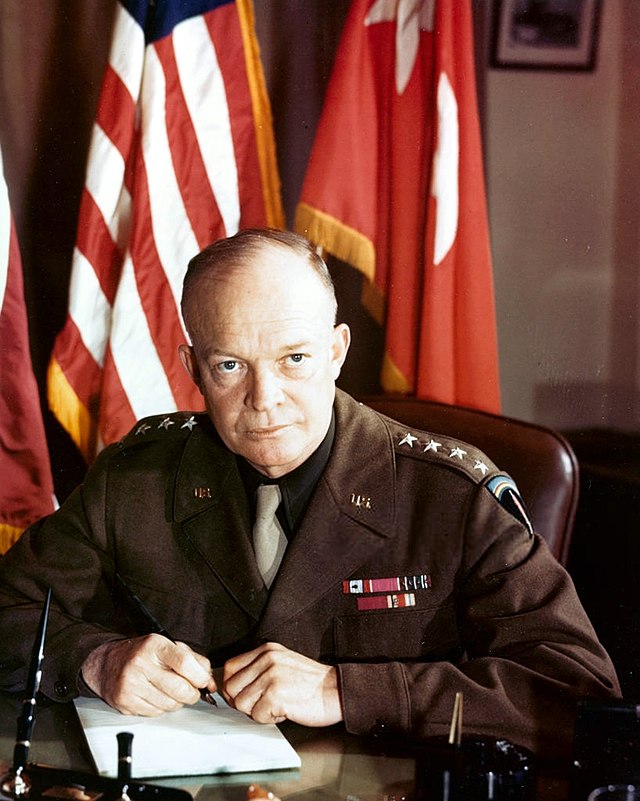 Photo of a balding older man in four-star general's uniform, seated in front of a USA flag